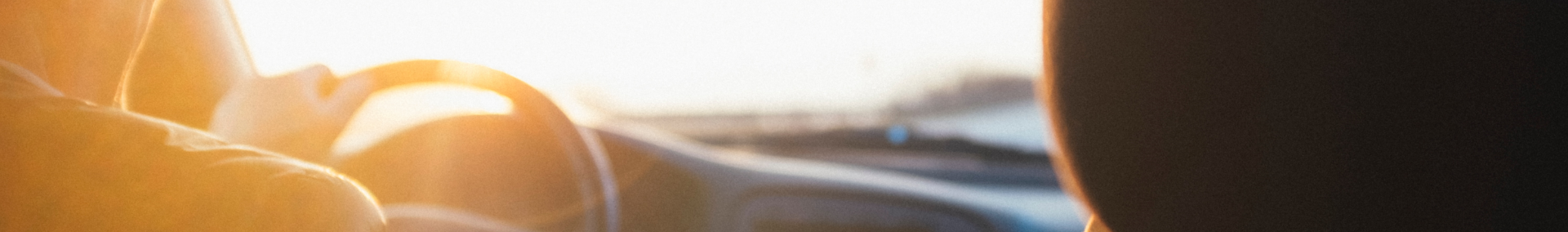 driver with one hand on steering wheel at sunset